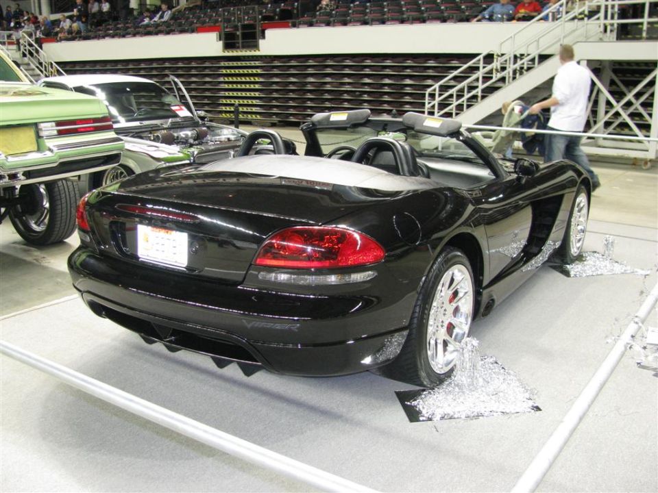 Black convertible sports car with a rear spoiler and chrome wheels, parked indoors