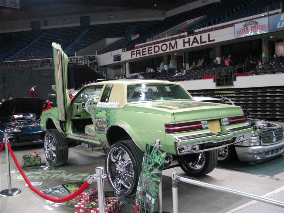 Customized light green coupe with gullwing doors and large chrome wheels, parked indoors