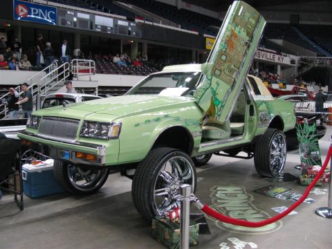2003 Mercury Marauder - A heavily modified sedan with custom paint and gullwing doors is displayed indoors at a car show.