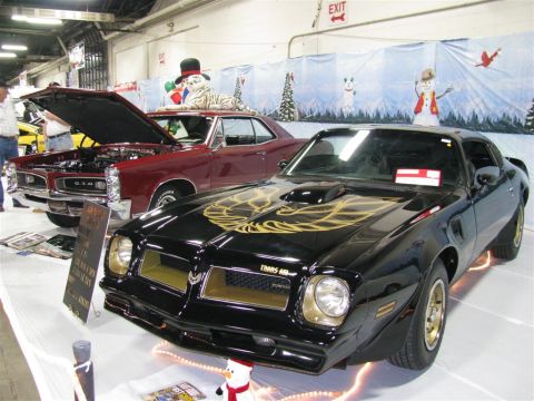 2003 Mercury Marauder - A black 1977 Pontiac Trans Am with gold decals is displayed at a car show next to a red Pontiac GTO.