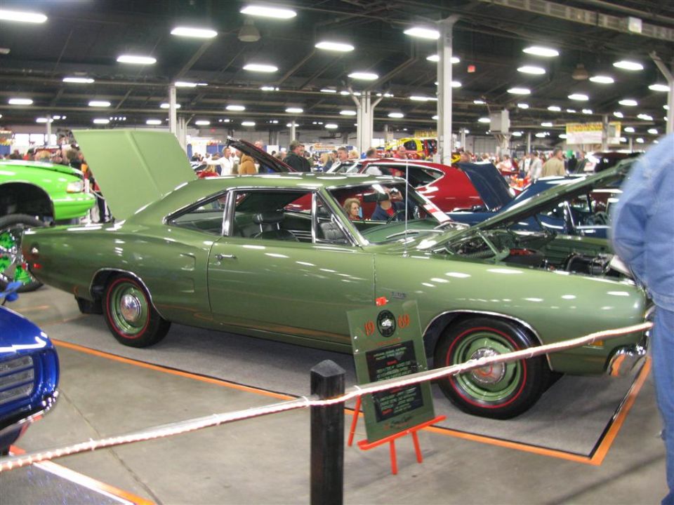 Green 1969 Dodge Super Bee with hood and trunk open at a car show. Other cars visible