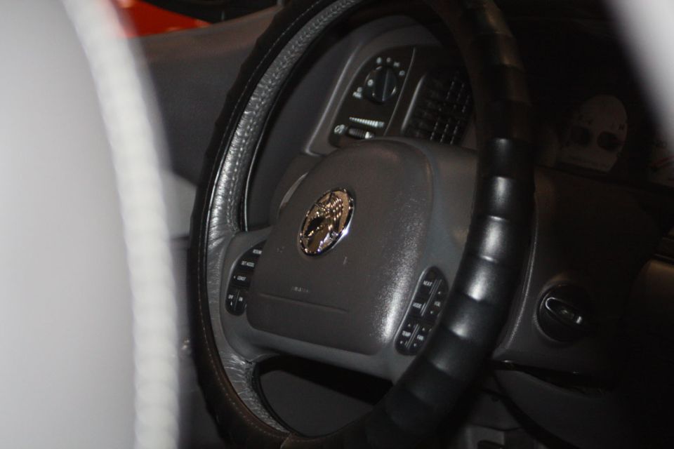 Interior shot of a car's steering wheel and dashboard. The steering wheel has a circular emblem in the center