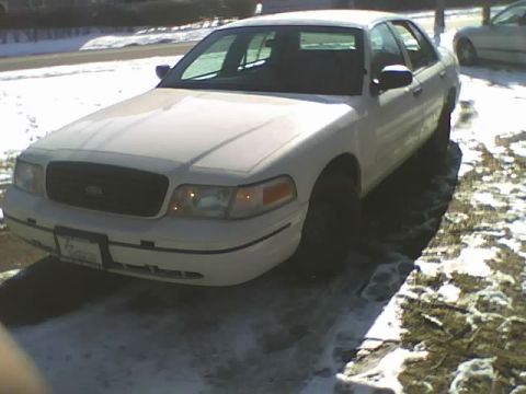 2000 Ford Crown Victoria - A white 2000 Ford Crown Victoria sedan is parked on a snowy surface, with another vehicle visible in the background.