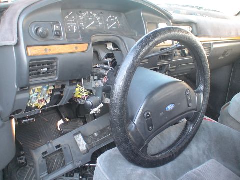 1993 Ford C-350 (Centurion Conversions) - The interior of a Ford truck shows a steering wheel and a dashboard with many components removed, revealing wiring and the fuse box.