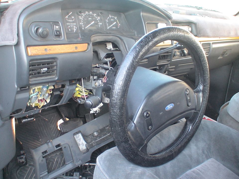 Ford truck dash with steering wheel removed, exposing column wiring and fuse panel
