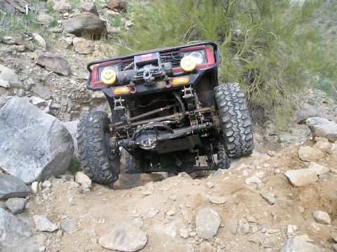 1986 Toyota Hilux - A modified red off-road vehicle tackles a challenging rocky trail with its front wheels angled.