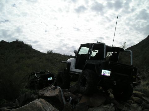 1986 Toyota Hilux - Two Jeeps navigate a rocky trail in a desert-like environment under a cloudy sky.