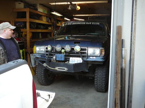 1991 Ford Bronco - A dark blue 1991 Ford Bronco is parked in a garage, modified for off-road use with a winch and extra lights.