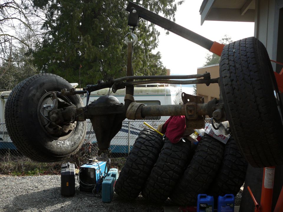 Vehicle axle assembly suspended by a shop crane, with spare tires stacked nearby