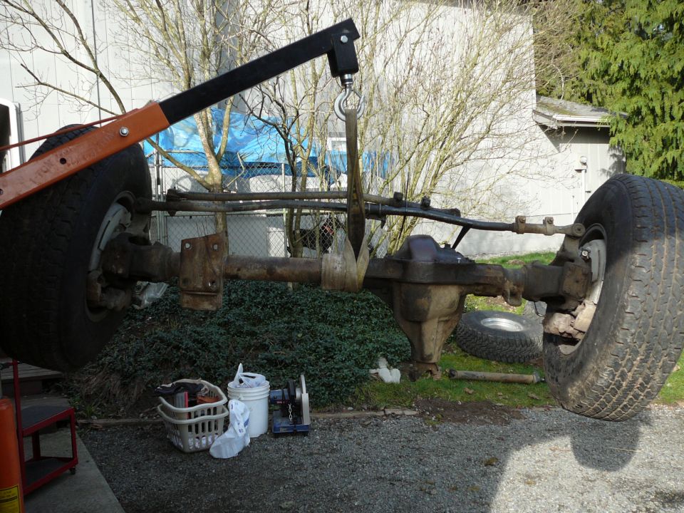 Ford Bronco front axle assembly suspended by an engine hoist, with large tires and suspension components visible