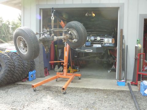 1991 Ford Bronco - The front axle and suspension of a 1990 Ford Bronco are suspended by a lift in a garage, with the truck visible in the background.