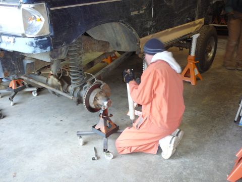 1991 Ford Bronco - A mechanic works on the suspension of a vehicle that is raised on jack stands in a garage.
