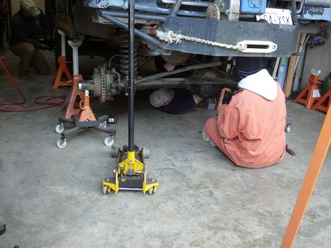 1991 Ford Bronco - Several people are working on the underside of a vehicle that is supported by jacks and jack stands.