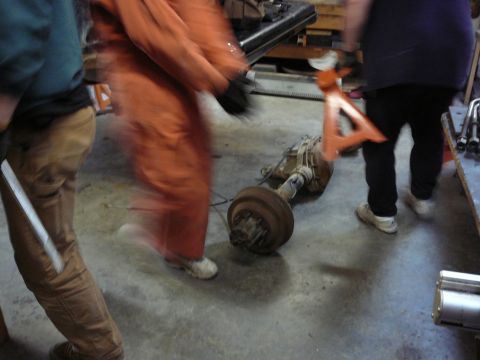 1991 Ford Bronco - An axle assembly is on the floor of a garage with people moving around it.