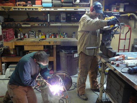 1991 Ford Bronco - Two men are working on vehicle parts in a garage, with one welding and the other using a grinder.