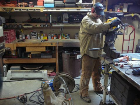 1991 Ford Bronco - A man is seen working in a cluttered workshop, utilizing a bench grinder amidst various tools and vehicle parts.