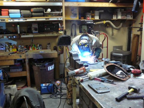1991 Ford Bronco - Workshop scene with a person welding metal parts and tools scattered on workbenches.