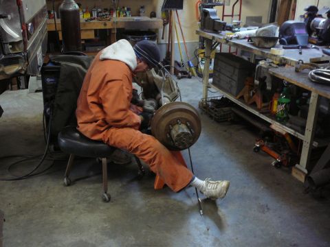 1991 Ford Bronco - A person is seated and working on a vehicle's axle assembly in a workshop environment.