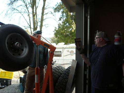 1991 Ford Bronco - Two men are working on a vehicle part in a garage setting, with an engine hoist and spare tire visible.