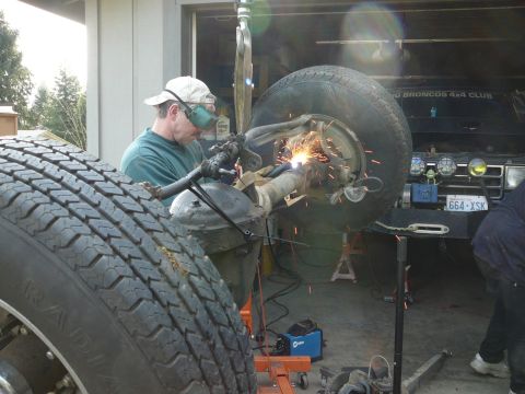 1991 Ford Bronco - A mechanic is welding a vehicle's axle while another vehicle sits nearby.