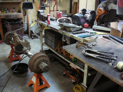 1991 Ford Bronco - A vehicle axle assembly is supported by jack stands in a cluttered garage workshop.