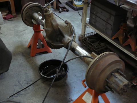 1991 Ford Bronco - A rusty rear axle assembly, likely from a truck or SUV, is supported by orange jack stands in a garage setting.