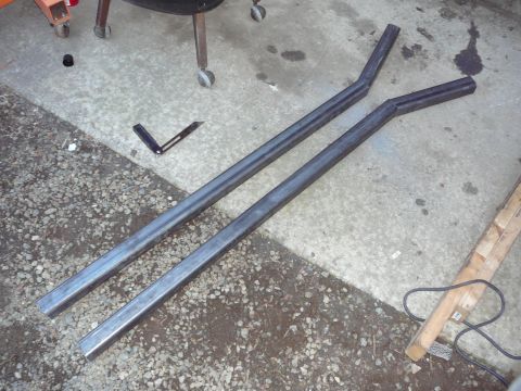 1991 Ford Bronco - Two custom metal tubes, possibly for a vehicle modification, lie on a concrete floor next to gravel.