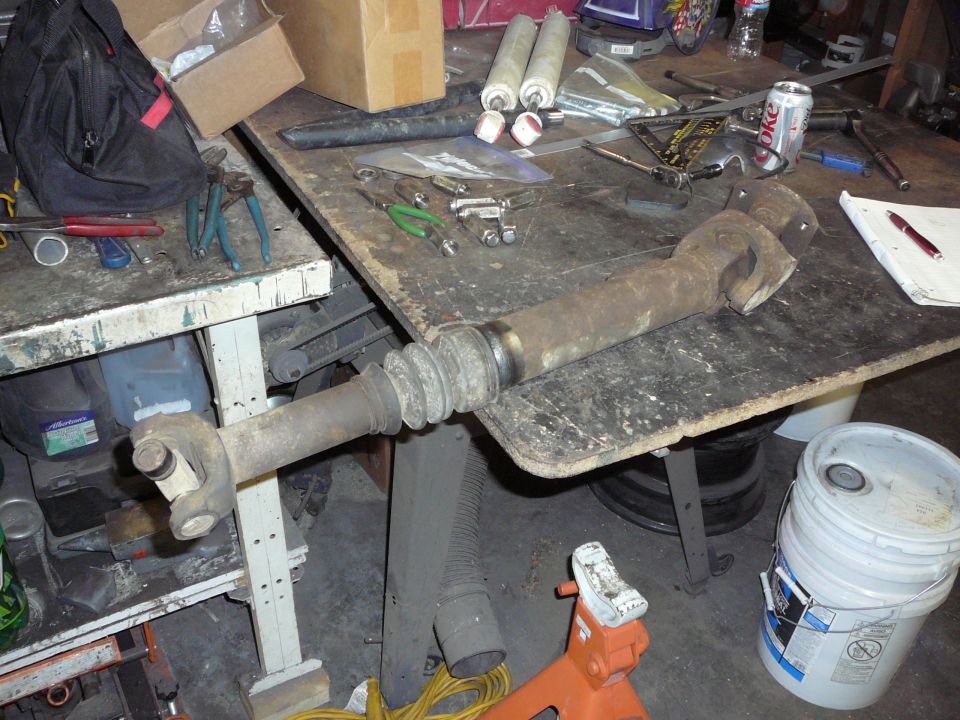 Driveshaft assembly with U-joints and rubber boot on a workbench with tools and parts