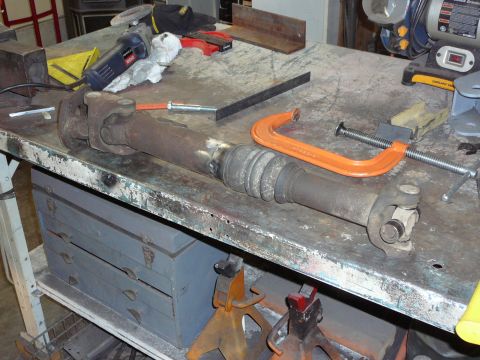1991 Ford Bronco - A driveshaft is clamped to a workbench, surrounded by tools and shop equipment.