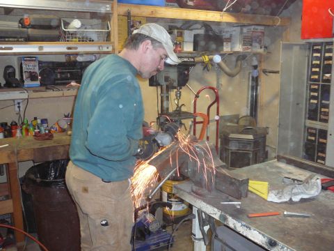 1991 Ford Bronco - A man is using an angle grinder on a piece of metal in a cluttered workshop.
