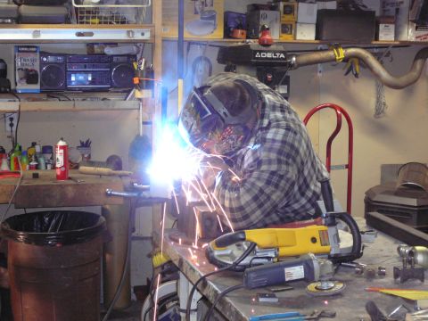 1991 Ford Bronco - Workshop scene with a person welding, surrounded by tools and various items on shelves and workbenches.