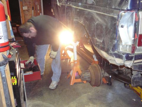 1991 Ford Bronco - A mechanic works on the rear of a damaged 1991 Ford Bronco in a garage.
