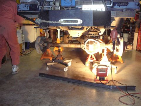 1991 Ford Bronco - Underbody view of a vehicle's axle and suspension components being worked on in a garage.