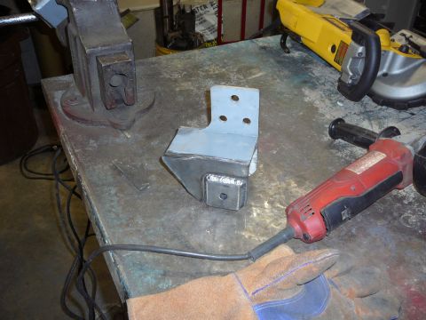 1991 Ford Bronco - A metal bracket sits on a workbench with tools, ready for fabrication.