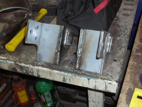 1991 Ford Bronco - Custom metal brackets sit on a cluttered workbench next to tools and a green bottle.