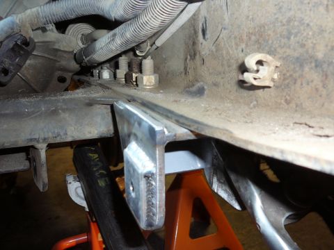 1991 Ford Bronco - A custom metal bracket is welded onto a rusty vehicle frame, which is supported by orange jack stands.