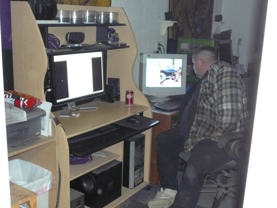 Man in plaid shirt looks at computer screen displaying a blue off-road vehicle