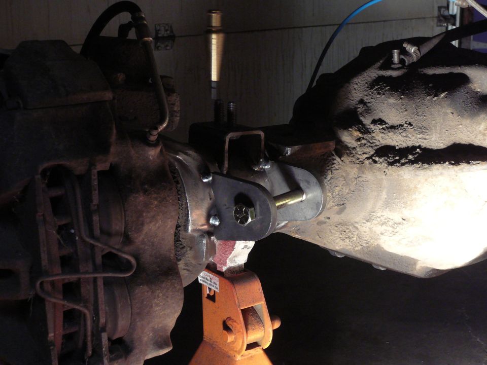 Custom suspension bracket welded to a vehicle axle, supported by an orange jack stand
