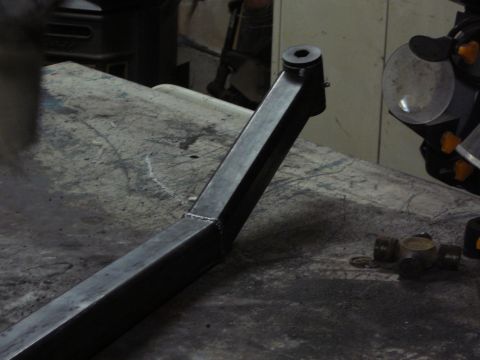 1991 Ford Bronco - A custom-fabricated metal part, likely for a vehicle's suspension, sits on a workbench next to a U-joint.
