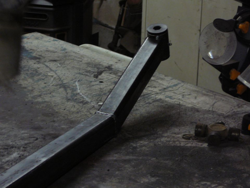 Close-up of a fabricated metal suspension component with a U-joint visible on a workbench