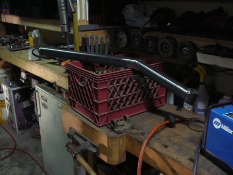 1991 Ford Bronco - A fabricated metal pipe sits on a workbench in a garage, next to tools and a welding machine.