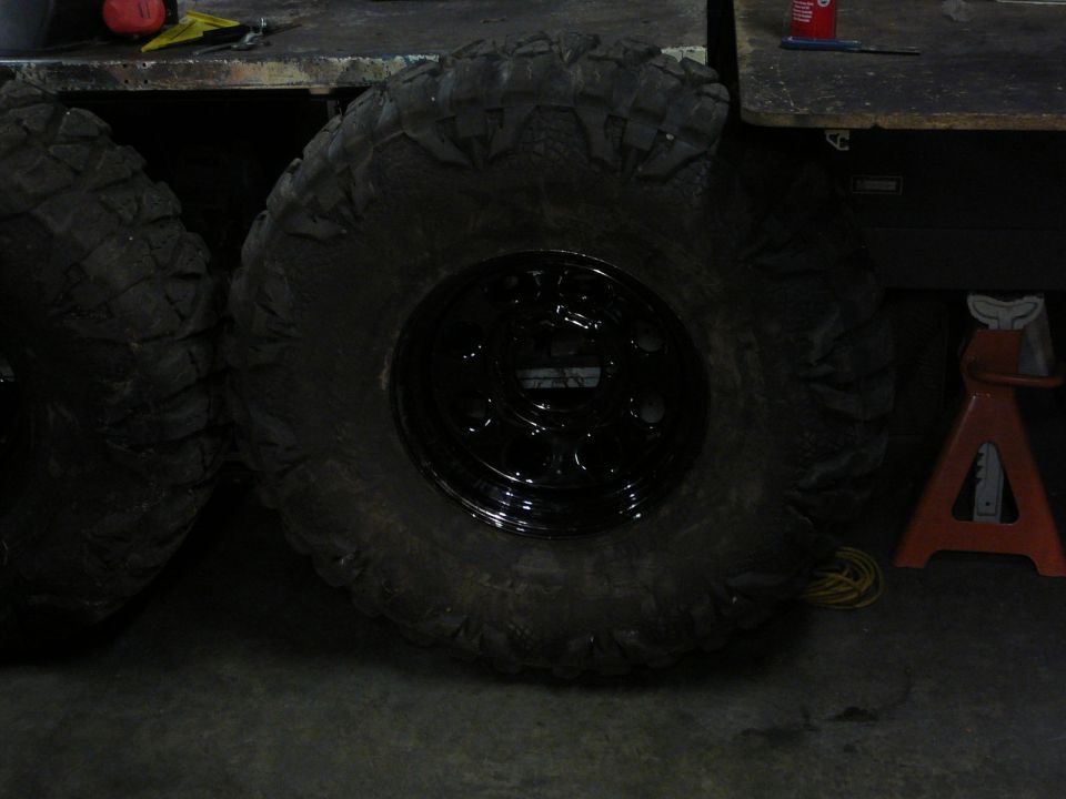 Black off-road tire and black rim on a concrete floor next to another tire