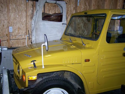 1988 Suzuki Samurai - Front quarter view of a yellow 1988 Suzuki Samurai, with a canvas cover visible behind it.