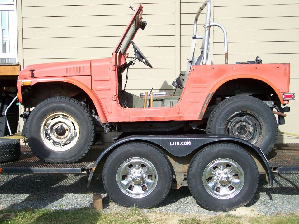 Side profile of weathered orange Suzuki LJ 4x4 with folded windshield on a tandem-axle trailer