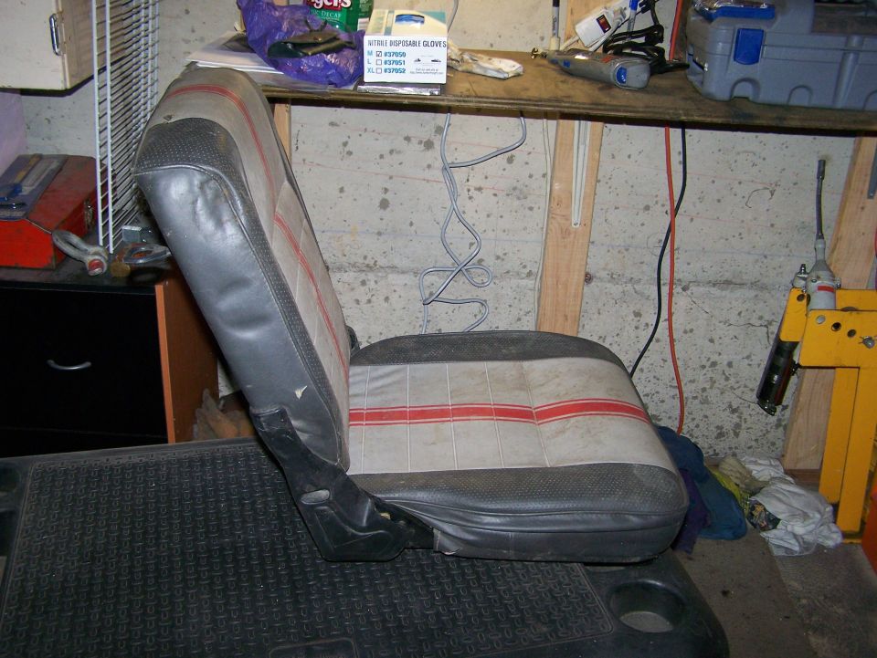 Car seat with grey, black, and red striped fabric, seen from the side in a workshop