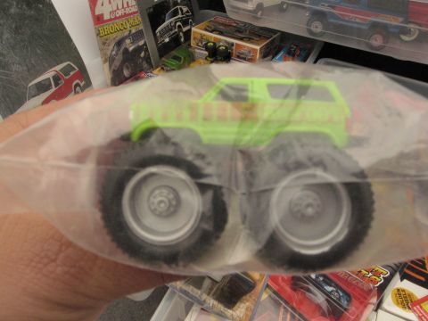 1986 Ford Bronco - A toy monster truck is shown in its packaging, with other toy vehicles and posters in the background.