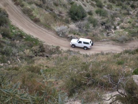 1979 Ford Bronco - A white SUV navigates a winding dirt road in a barren, hilly terrain.