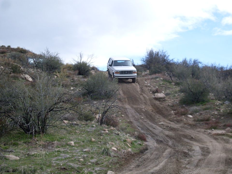 White 1992 Ford Bronco climbing a steep dirt trail with scrub brush and rocks