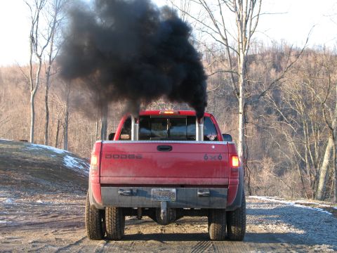 1985 Ford Bronco - A red Dodge 6x6 pickup truck is seen from the rear, expelling a large cloud of black exhaust smoke.