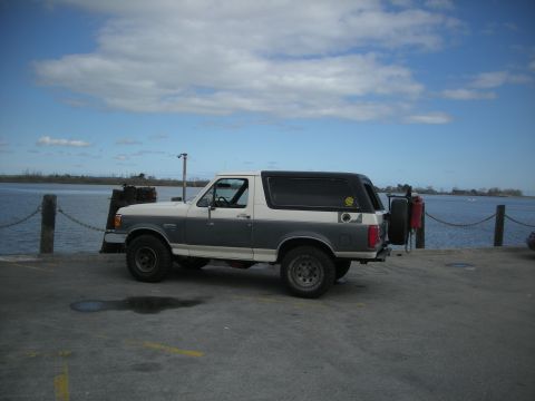 1991 Ford Bronco - A two-tone Ford Bronco is parked near a body of water under a cloudy sky.